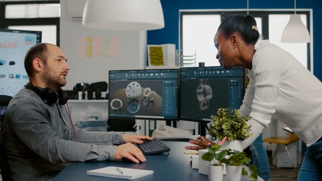 Group of engineers discussing ideas for electric bicycle in the office with 3D modelling software showing on the monitor.
